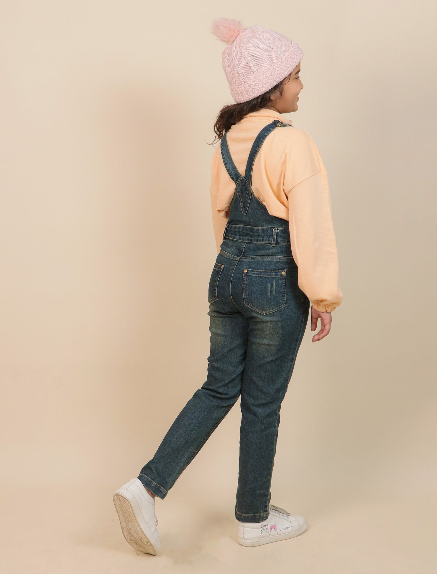 Girls wearing denim overalls and a pink beanie on a beige background