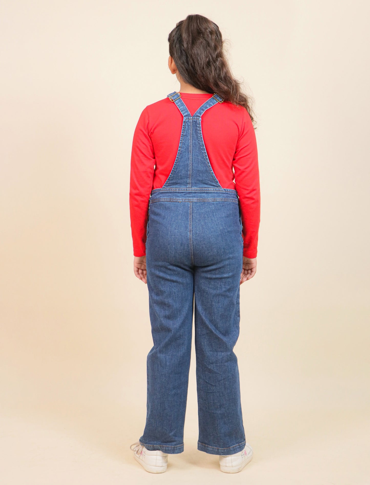 Girls wearing blue denim overalls and a red shirt on a beige background