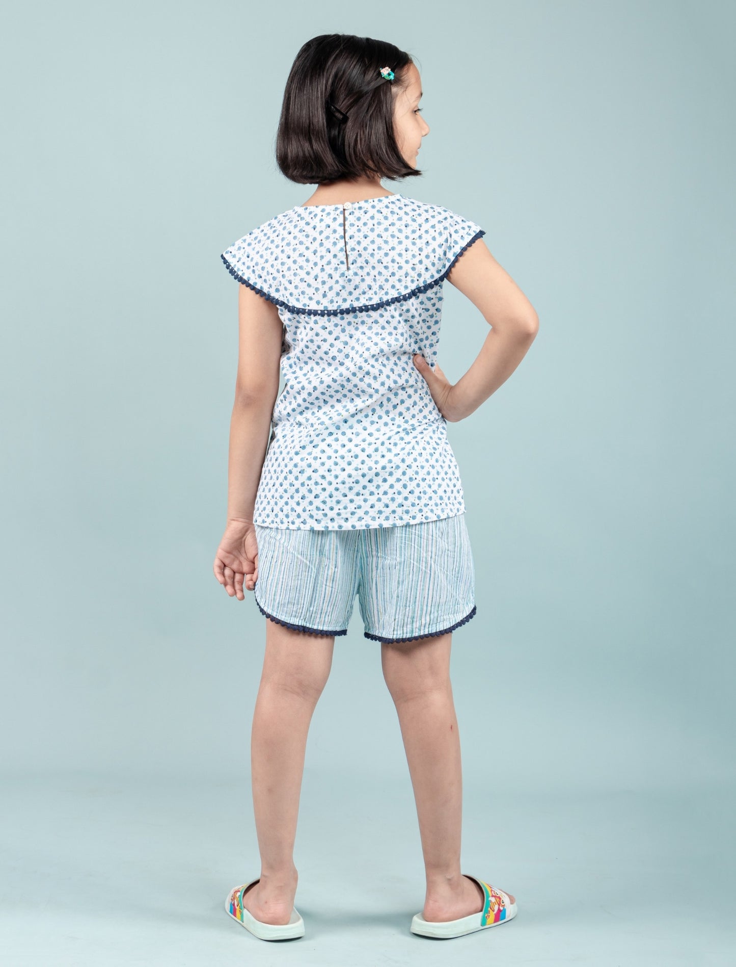 Girl wearing blue block printed nightdress set with shorts and floral top, back view