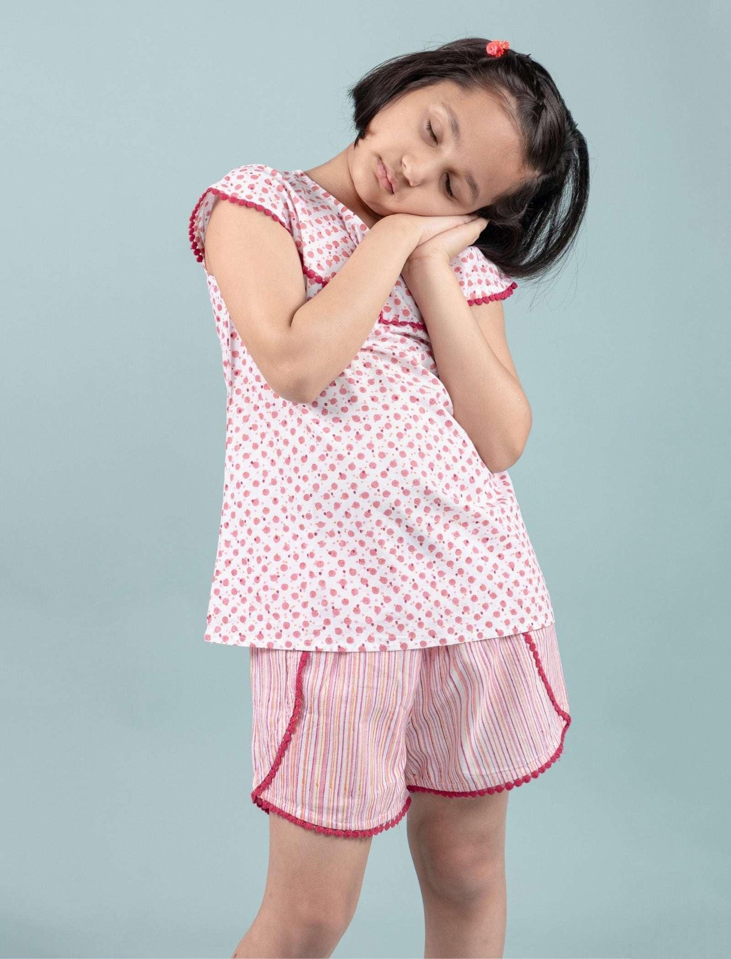 Girl in printed nightdress set with cap sleeves and striped shorts, posing with sleepy gesture