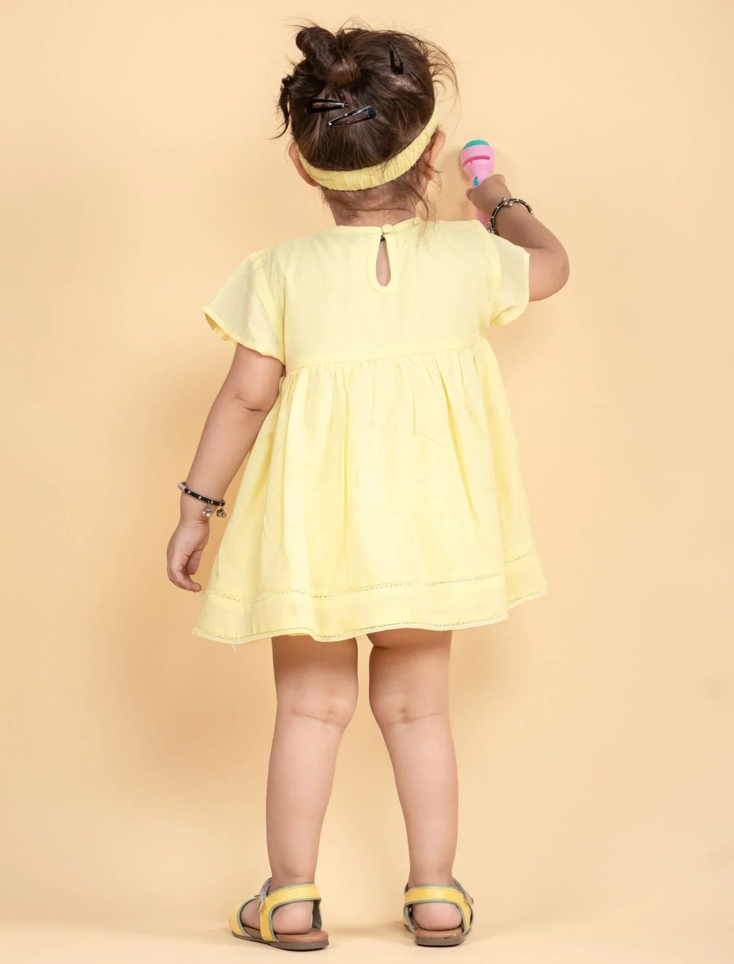 Toddler girl in a light yellow summer frock with headband and sandals, facing away