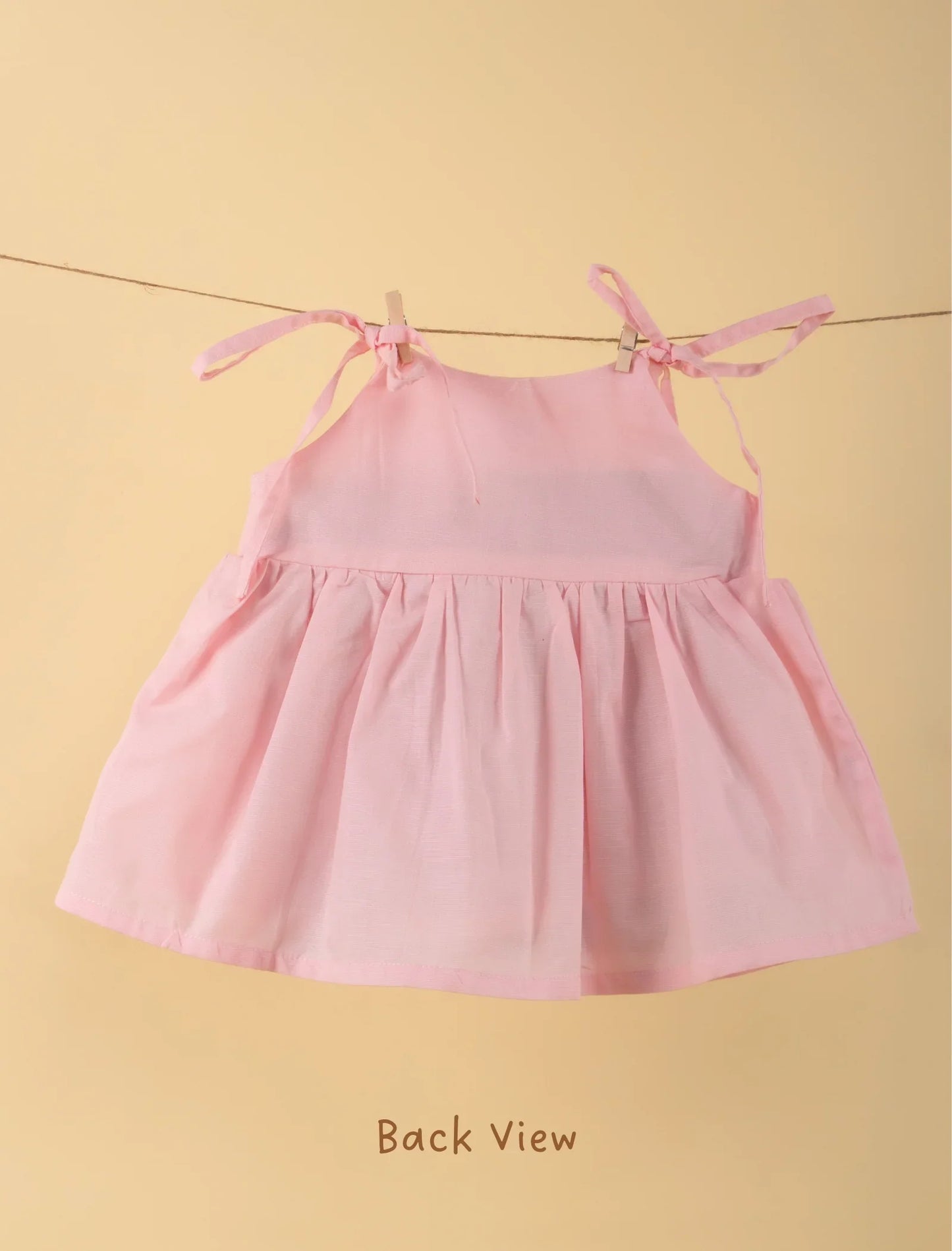 Back view of a light pink sleeveless newborn baby girl frock with shoulder tie straps