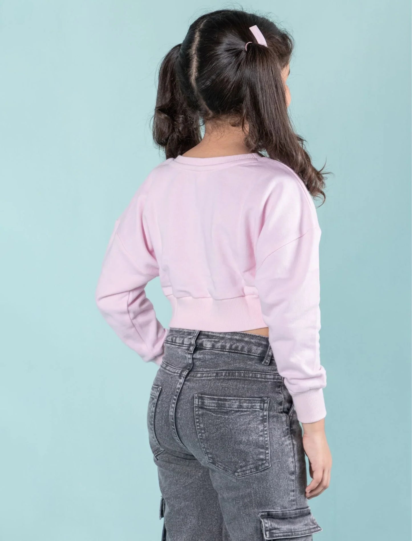 Girl wearing light pink sweatshirt and gray denim jeans, standing against blue background