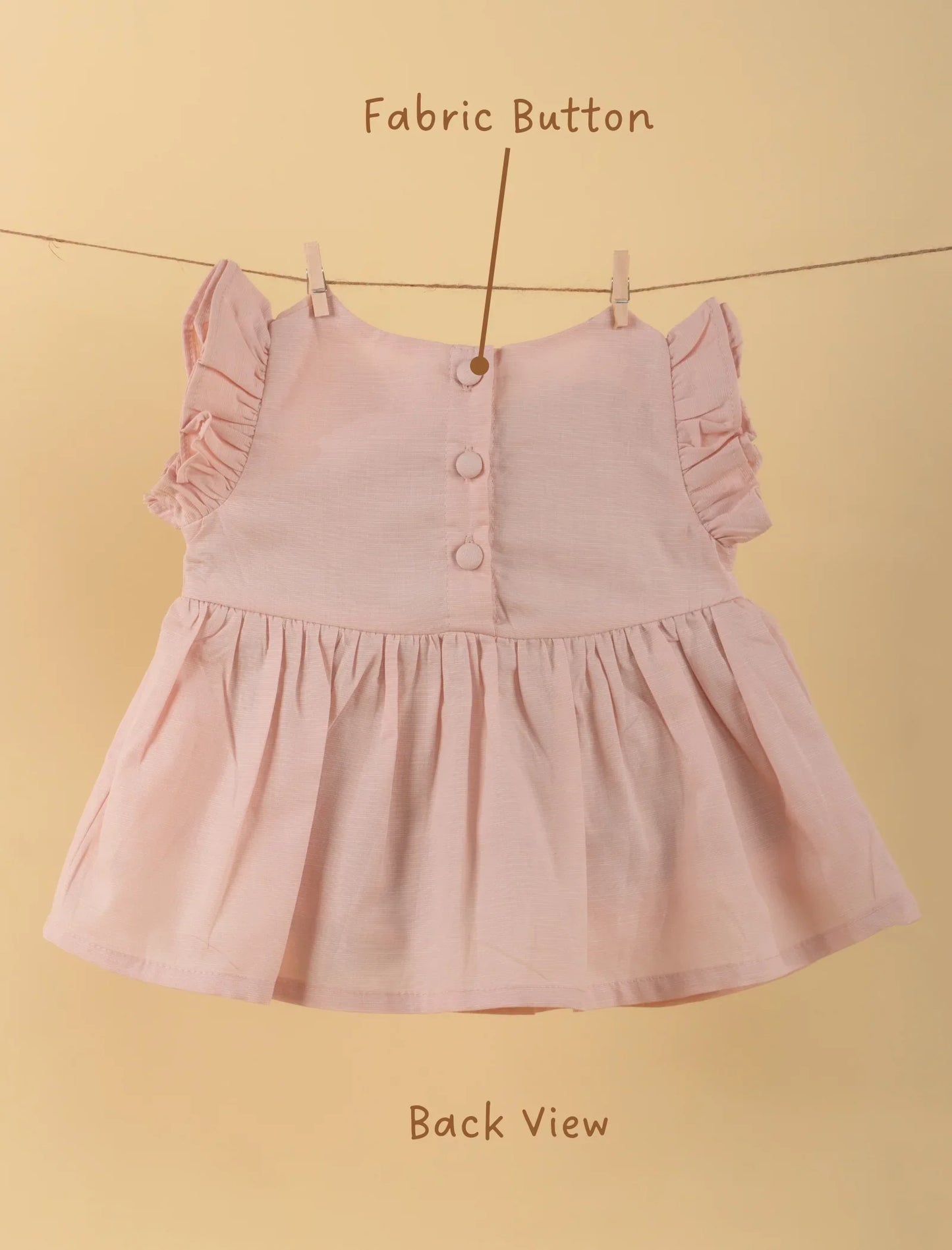 Back view of pink baby dress with ruffle sleeves and fabric buttons on beige background