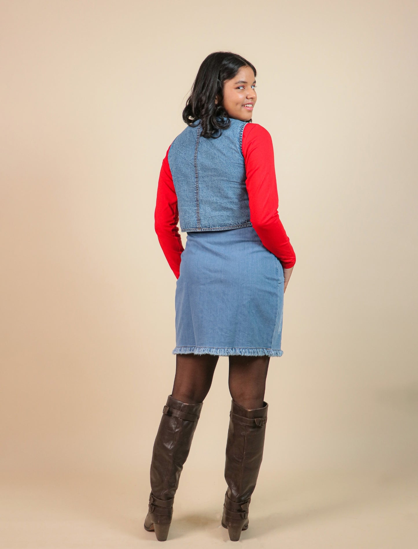 Girls wearing a denim outfit with a red sweater and brown knee-high boots on a beige background