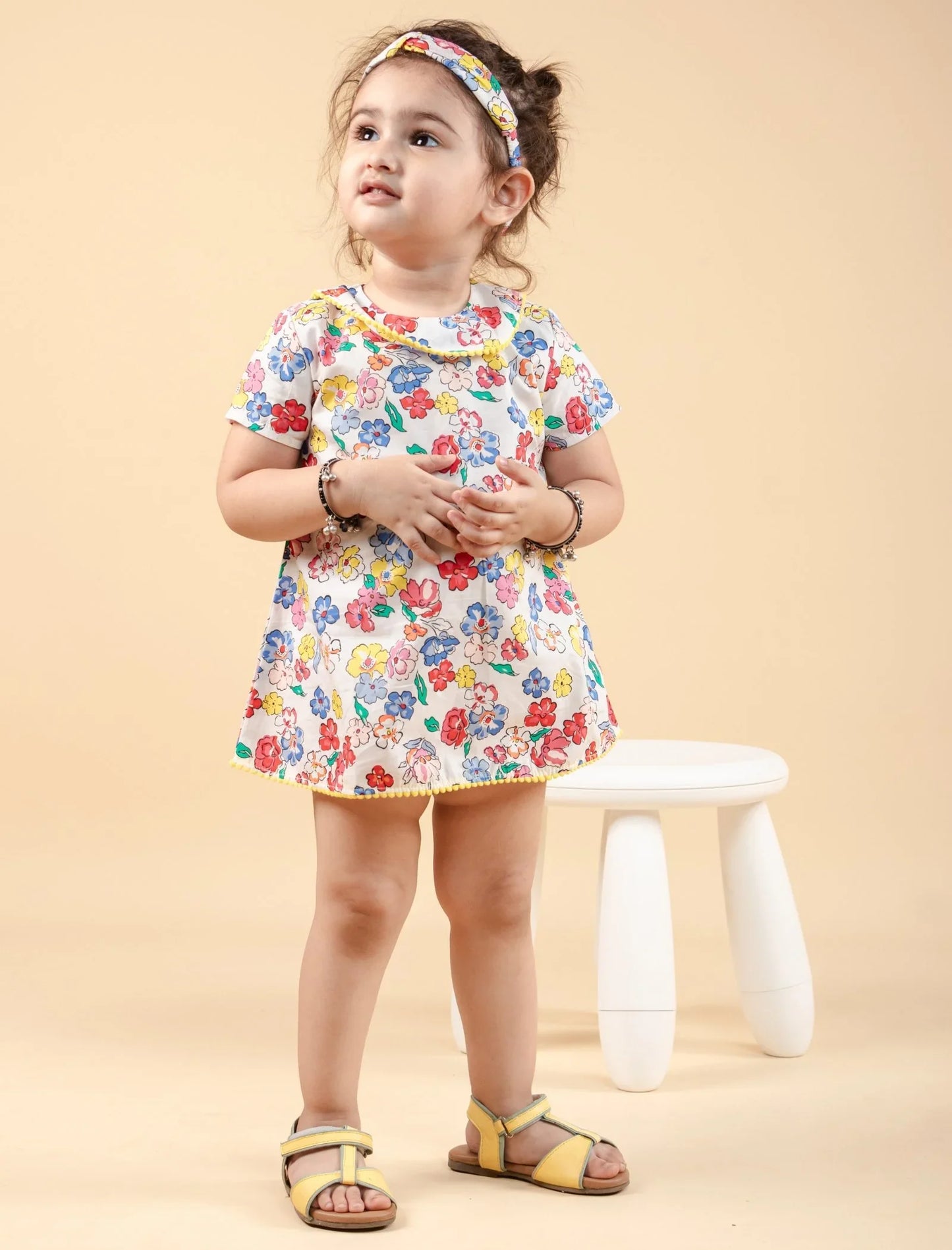 Little girl in a colorful floral dress and matching headband, standing indoors