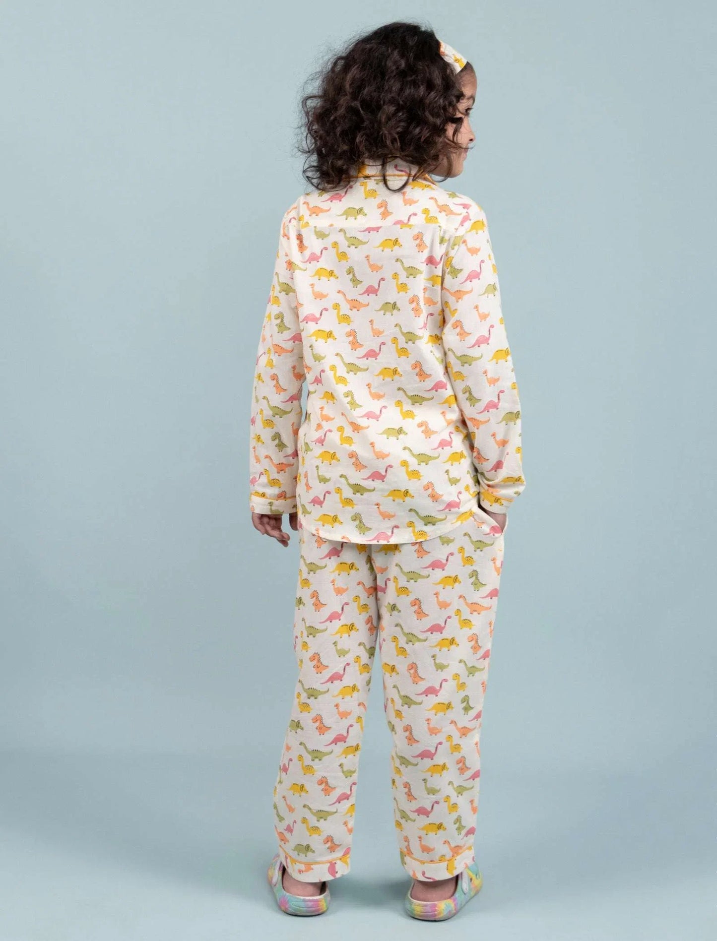 Girl wearing colorful dinosaur print pajama set and matching headband, back view