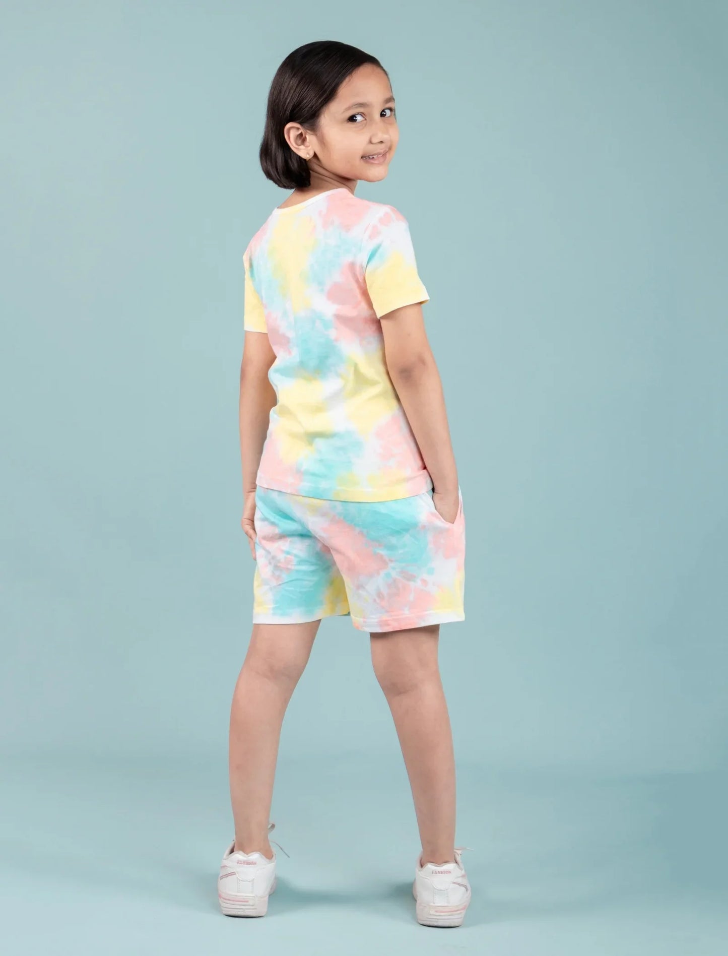 Girl wearing pastel tie-dye night suit set with shorts, standing against a light blue background