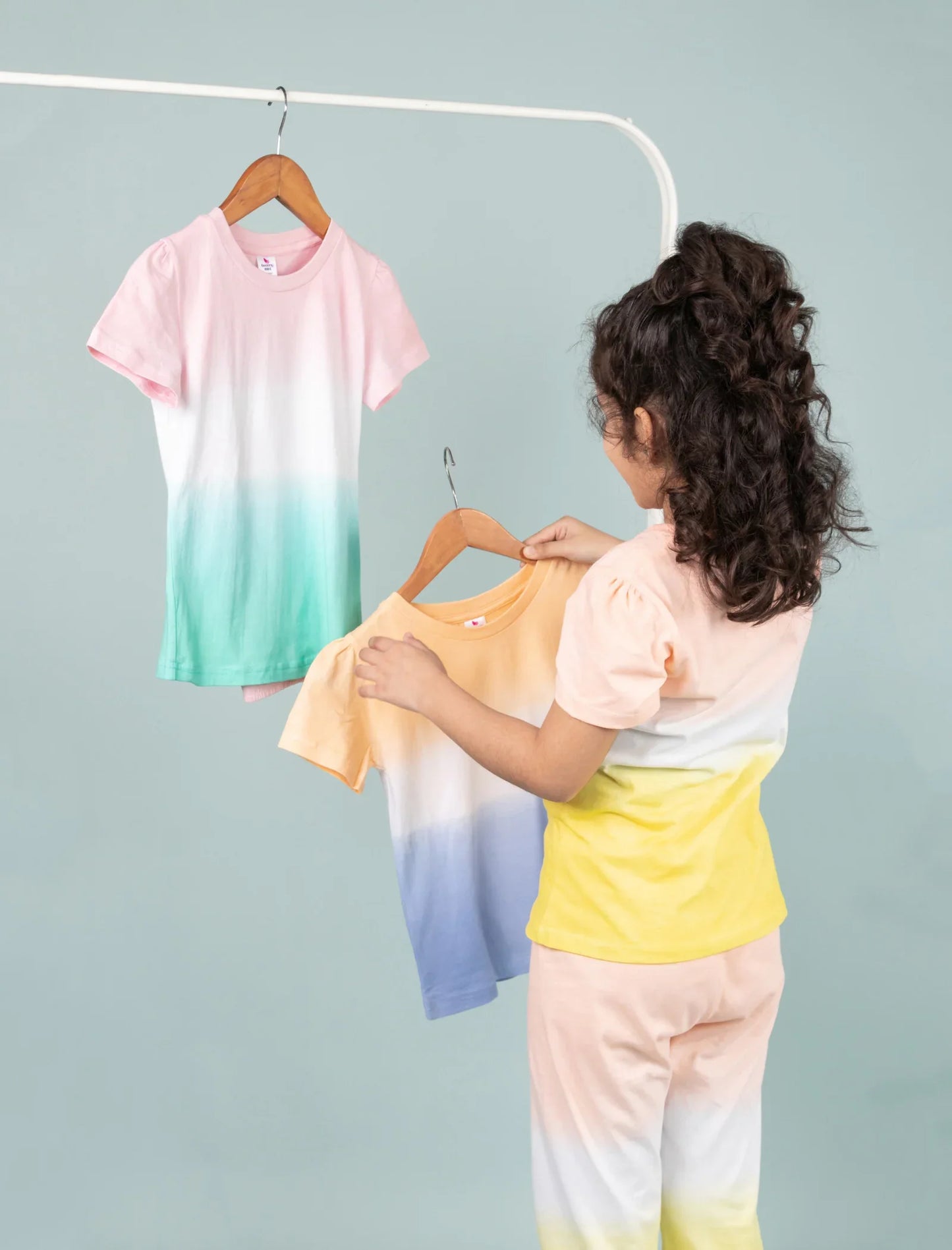 Girl in pastel tie-dye night suit holding another colorful tie-dye girls' nightwear set