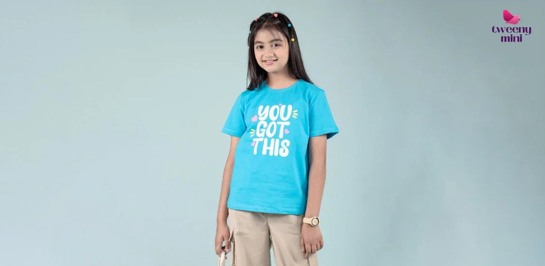 Smiling girl wearing blue graphic t-shirt and beige pants, kids fashion photoshoot