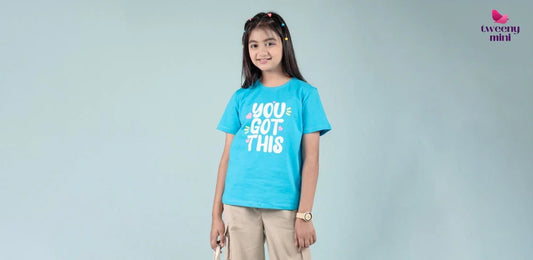 Smiling girl wearing blue graphic t-shirt and beige pants, kids fashion photoshoot