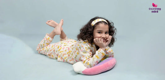 Smiling girl in printed night suit set with matching headband lying on pastel pillow