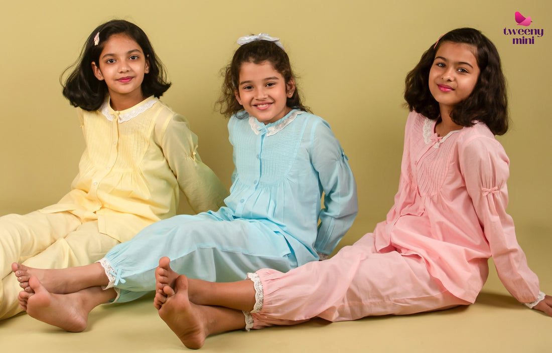 Three young girls in pastel nightwear sitting on the floor, smiling against a plain background.