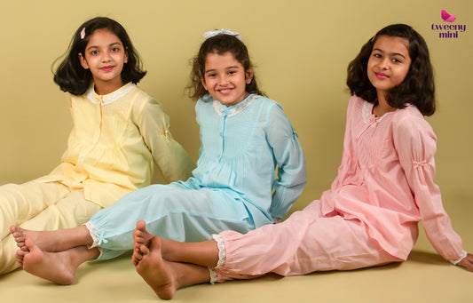 Three young girls in pastel nightwear sitting on the floor, smiling against a plain background.