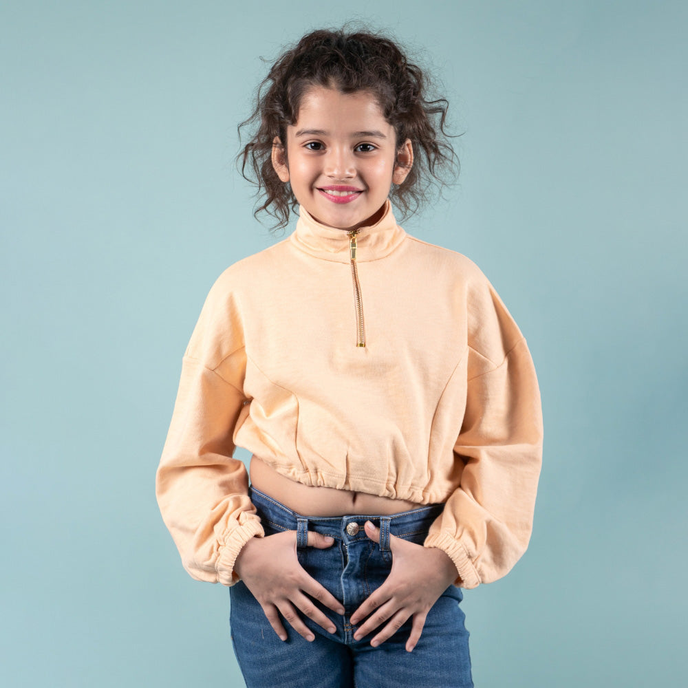 Smiling girl in peach cropped sweatshirt and blue jeans, kids fashion apparel on blue background