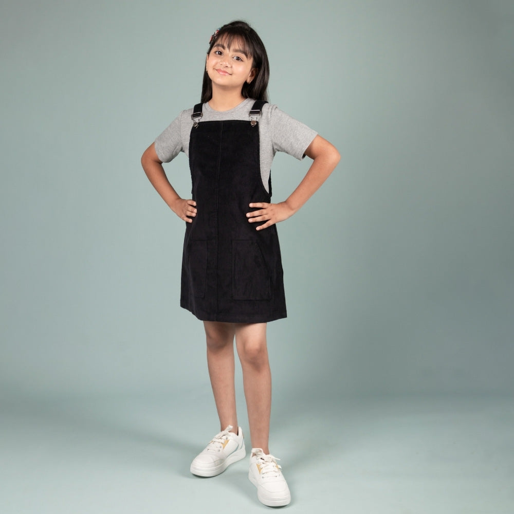 Smiling girl in black dungaree dress and grey t-shirt, posing on light background