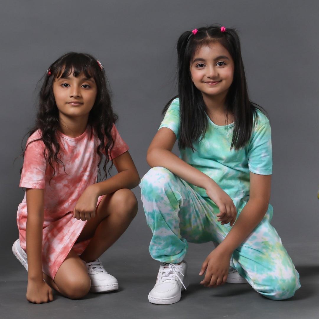 Two girls in colorful tie-dye kidswear posing against a plain grey background