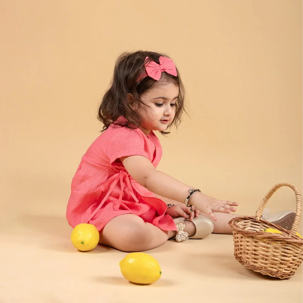 Baby girl in a pink dress and bow headband sitting with lemons and a wicker basket on beige background