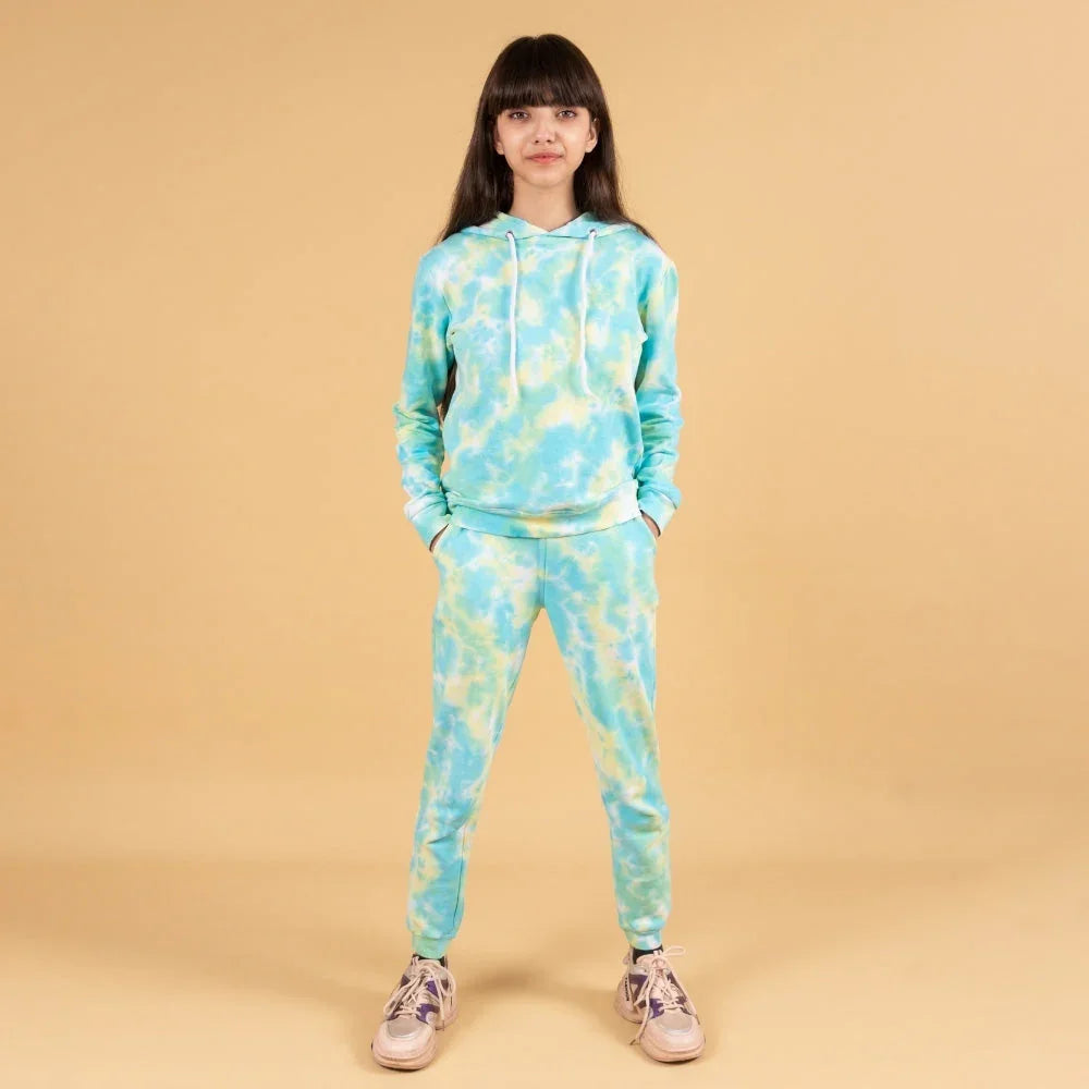 Girl wearing blue and yellow tie-dye jogger set with hoodie and sneakers on beige backdrop