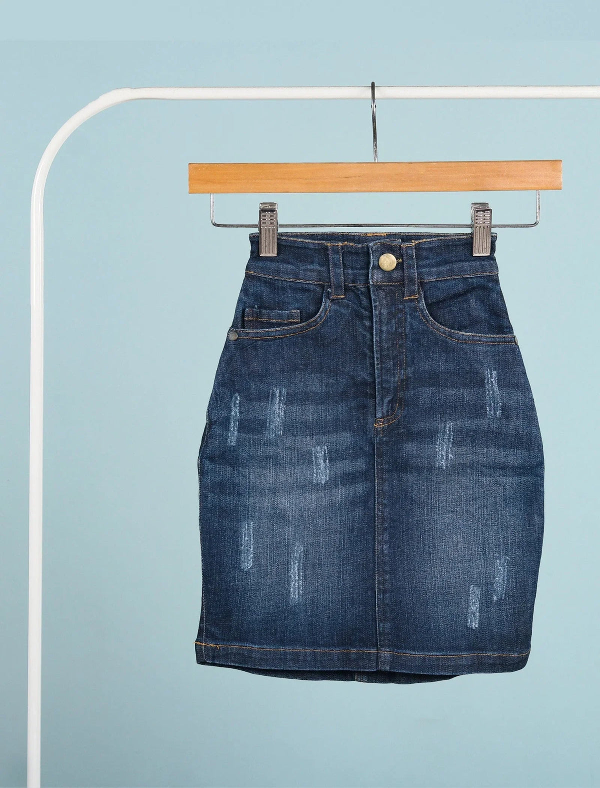 Blue denim skirt for girls age 7, high-waisted with distressed details, hanging on hanger