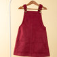 Red pinafore dress on a hanger against a beige background