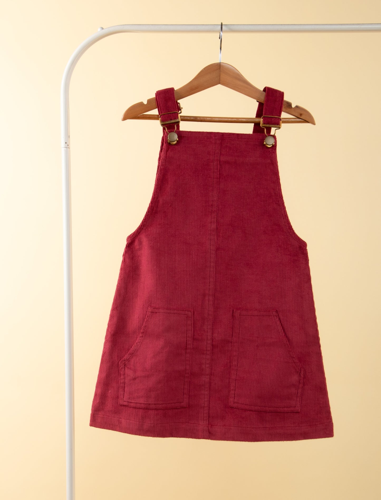 Red pinafore dress on a hanger against a beige background