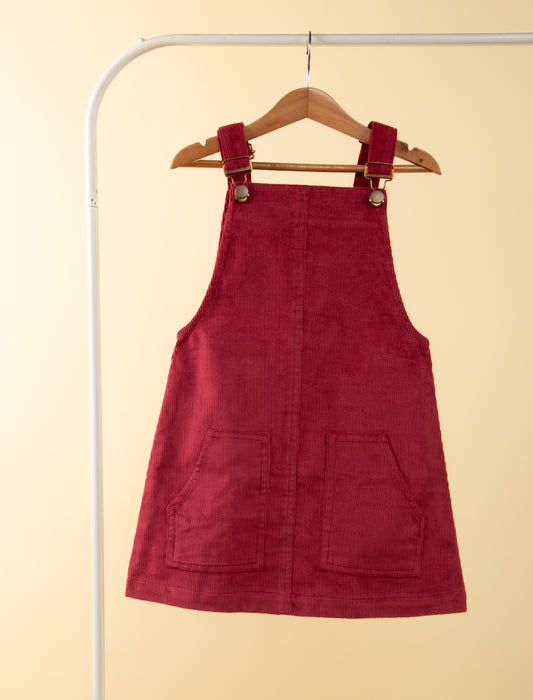 Red pinafore dress on a hanger against a beige background