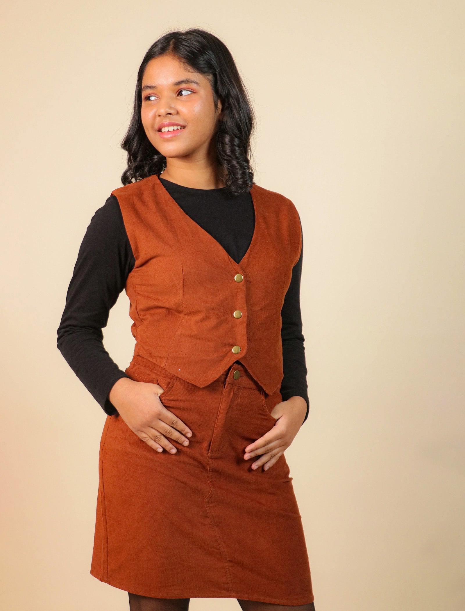 Girls wearing a brown vest over a black shirt on a beige background