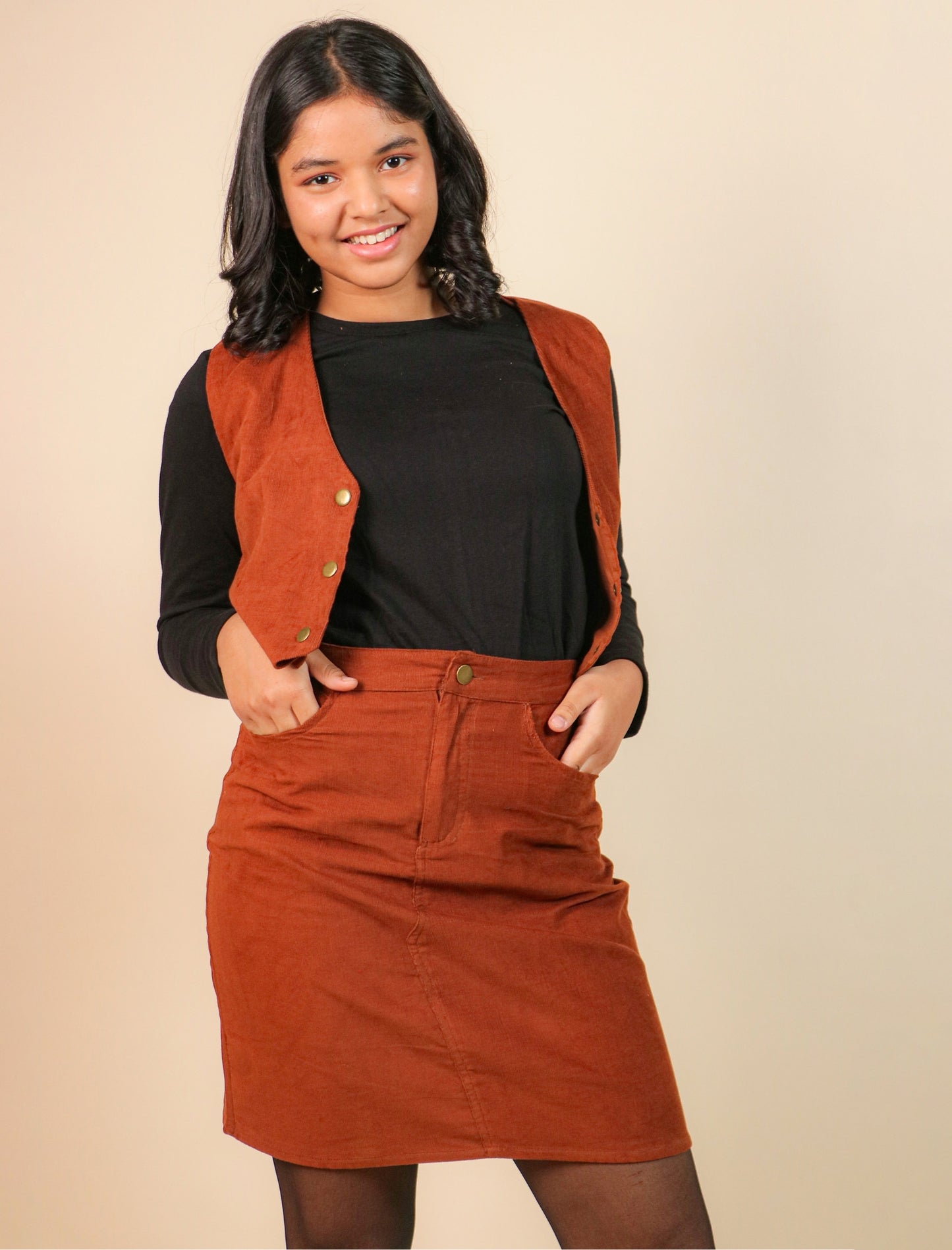 Girls wearing a brown vest over a black top and skirt on a beige background