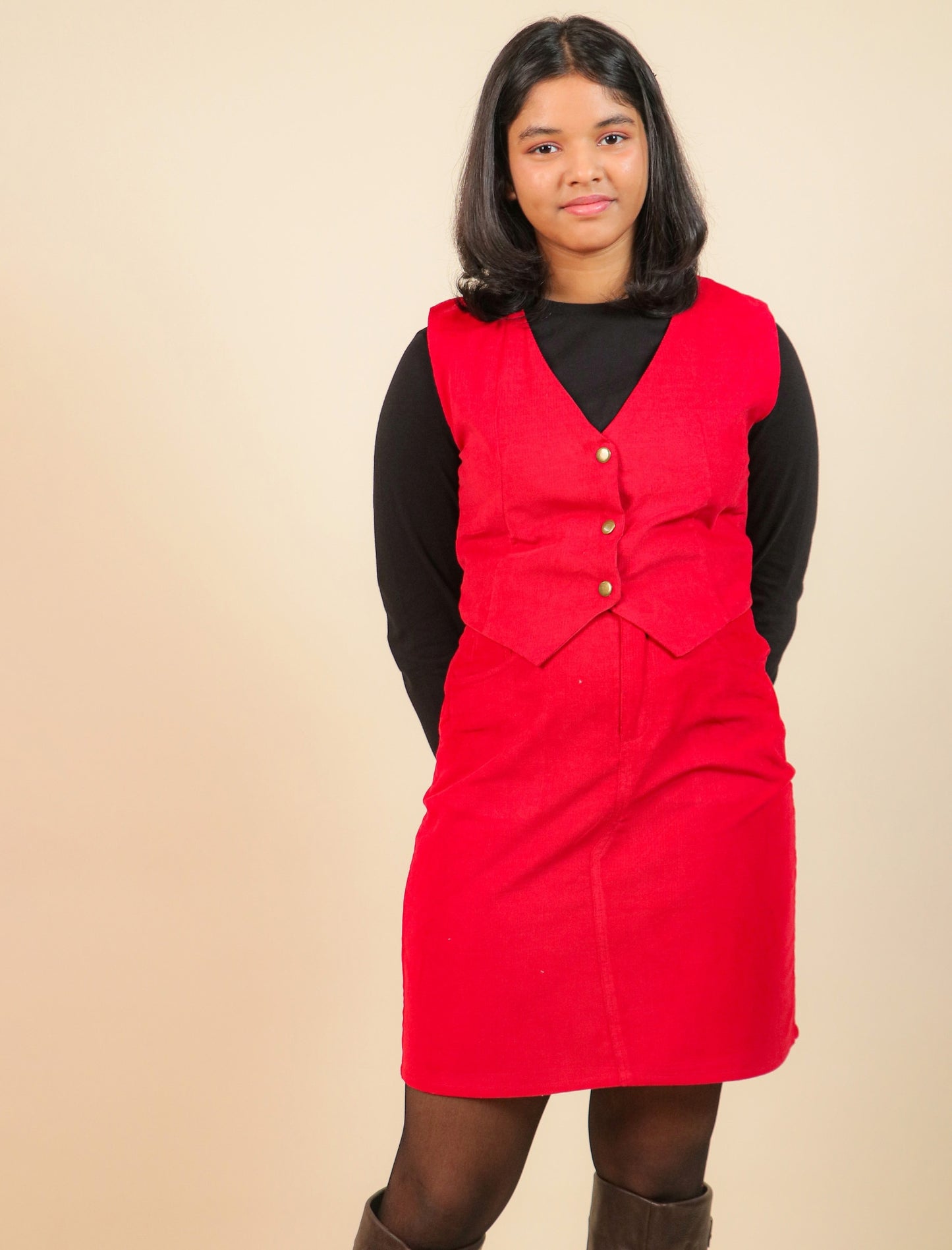Girls wearing a red dress with a vest over a black shirt on a beige background