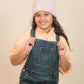 girls wearing a pink knit hat and denim overalls against a beige background