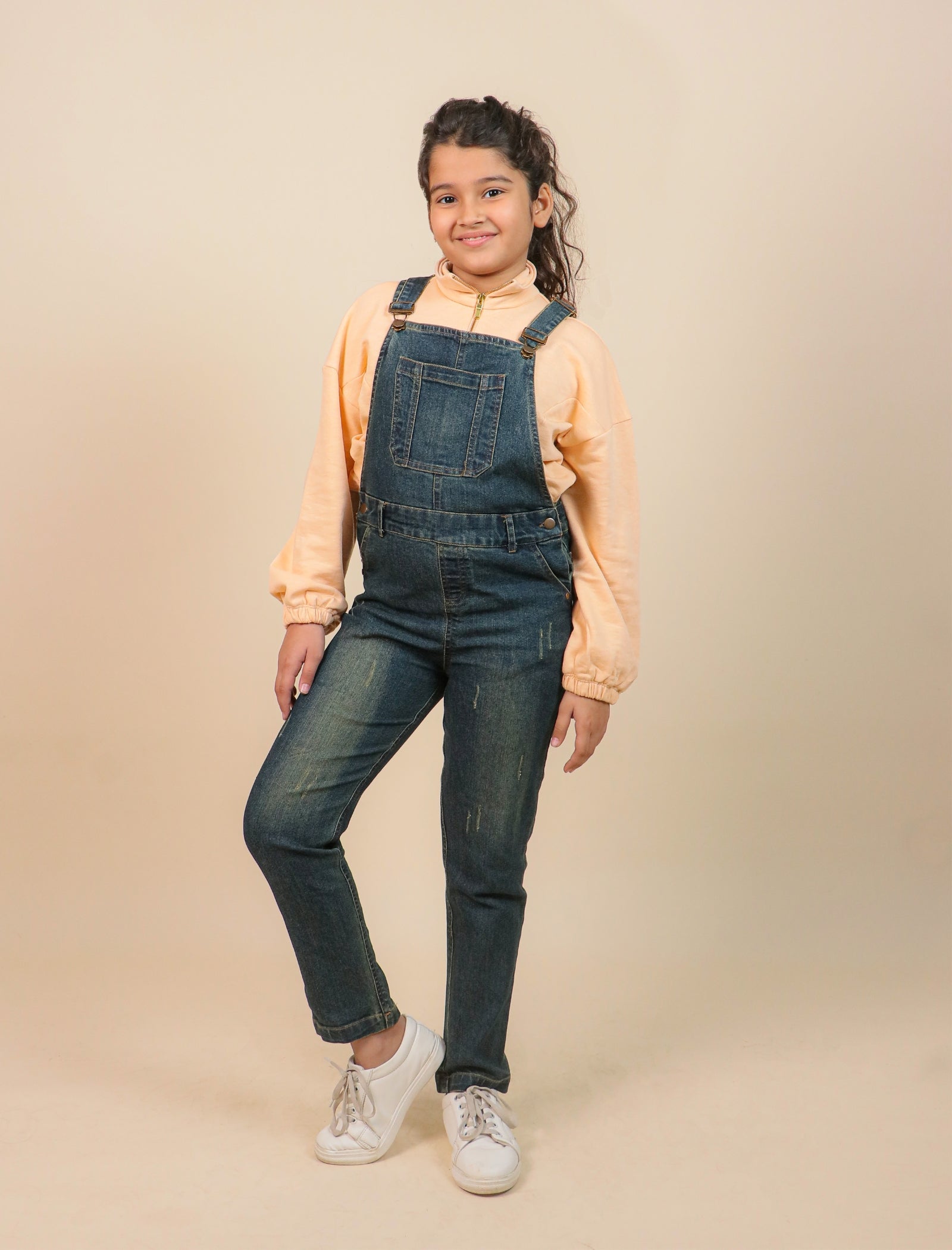 Girls wearing denim overalls and a light-colored shirt on a beige background