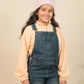 Girls wearing a pink beanie and denim overalls against a beige background
