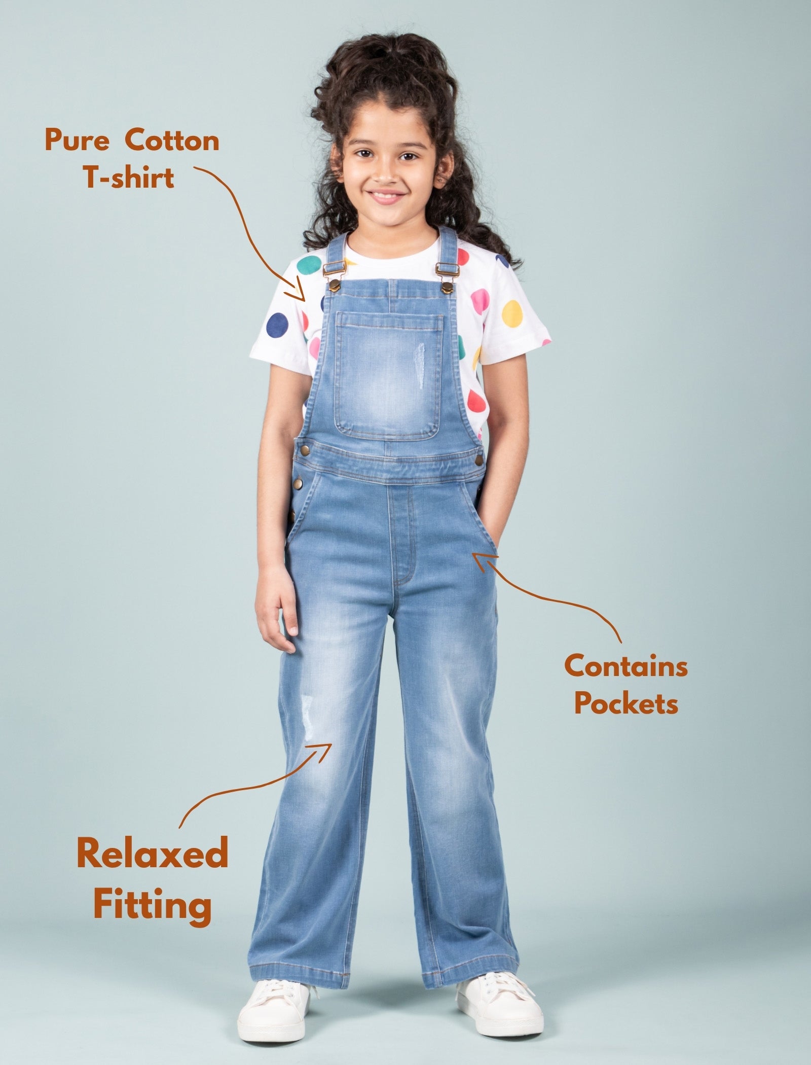 Child wearing a white t-shirt with colorful polka dots and blue denim overalls on a light gray background.