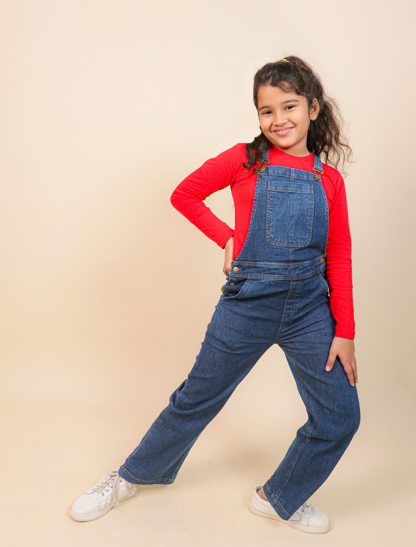 Girls wearing a red shirt and blue denim overalls on a beige background