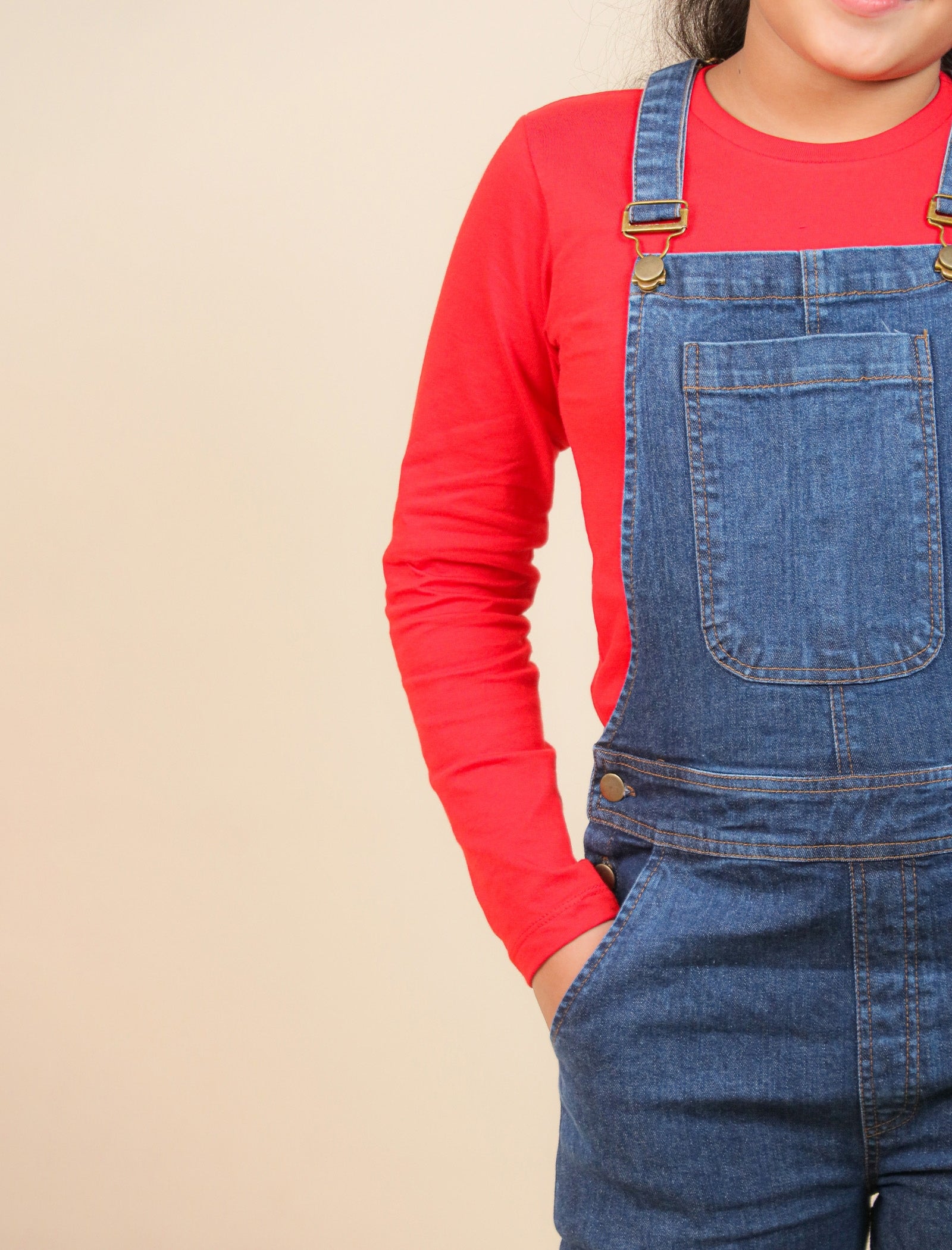 Girls wearing a red long-sleeve shirt and blue denim overalls on a beige background