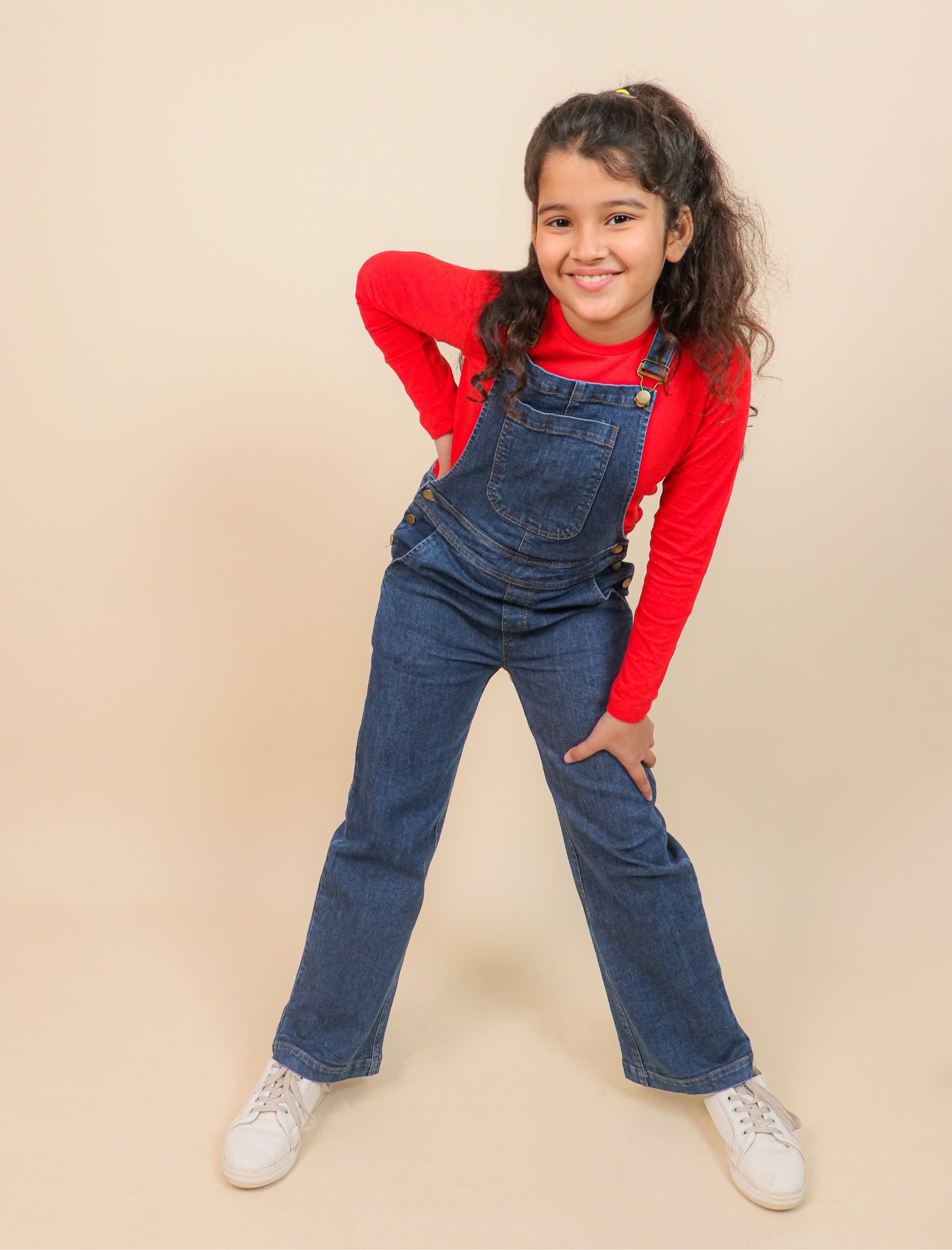 Girls wearing blue denim overalls and a red shirt on a beige background