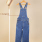 Blue denim dungaree on a hanger against a beige background