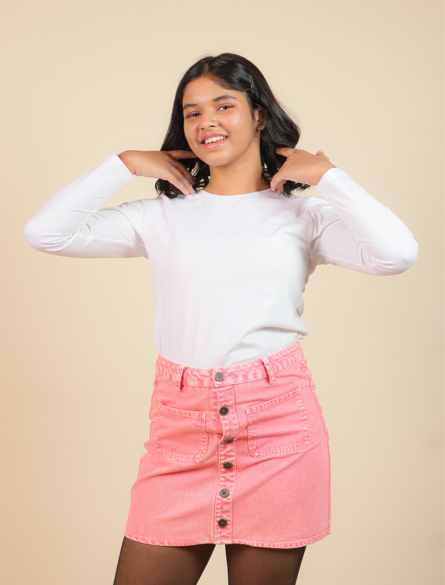 girls wearing a white long-sleeve top and pink denim skirt against a beige background