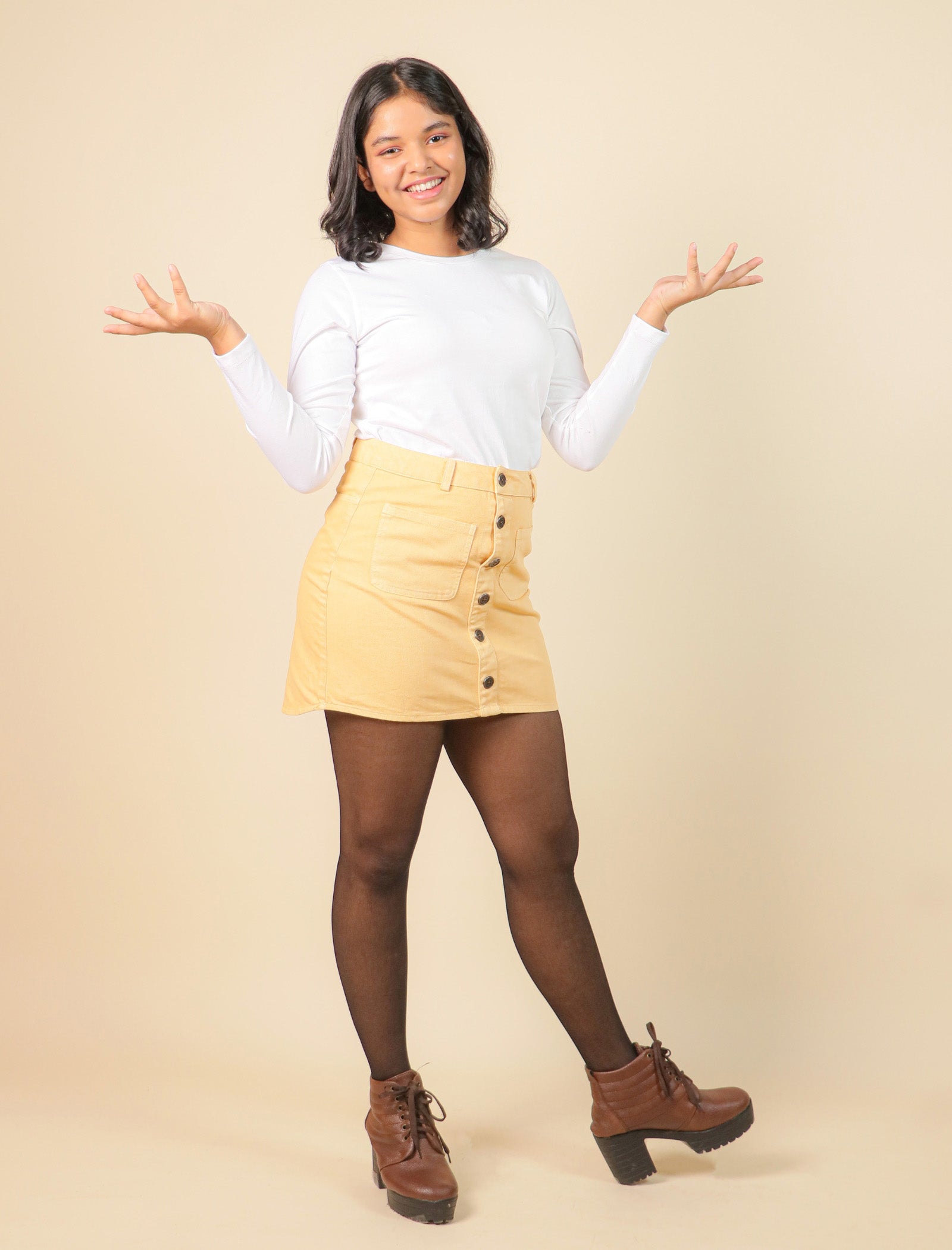 Girls wearing a white long-sleeve top, beige button-up skirt, and brown boots on a beige background