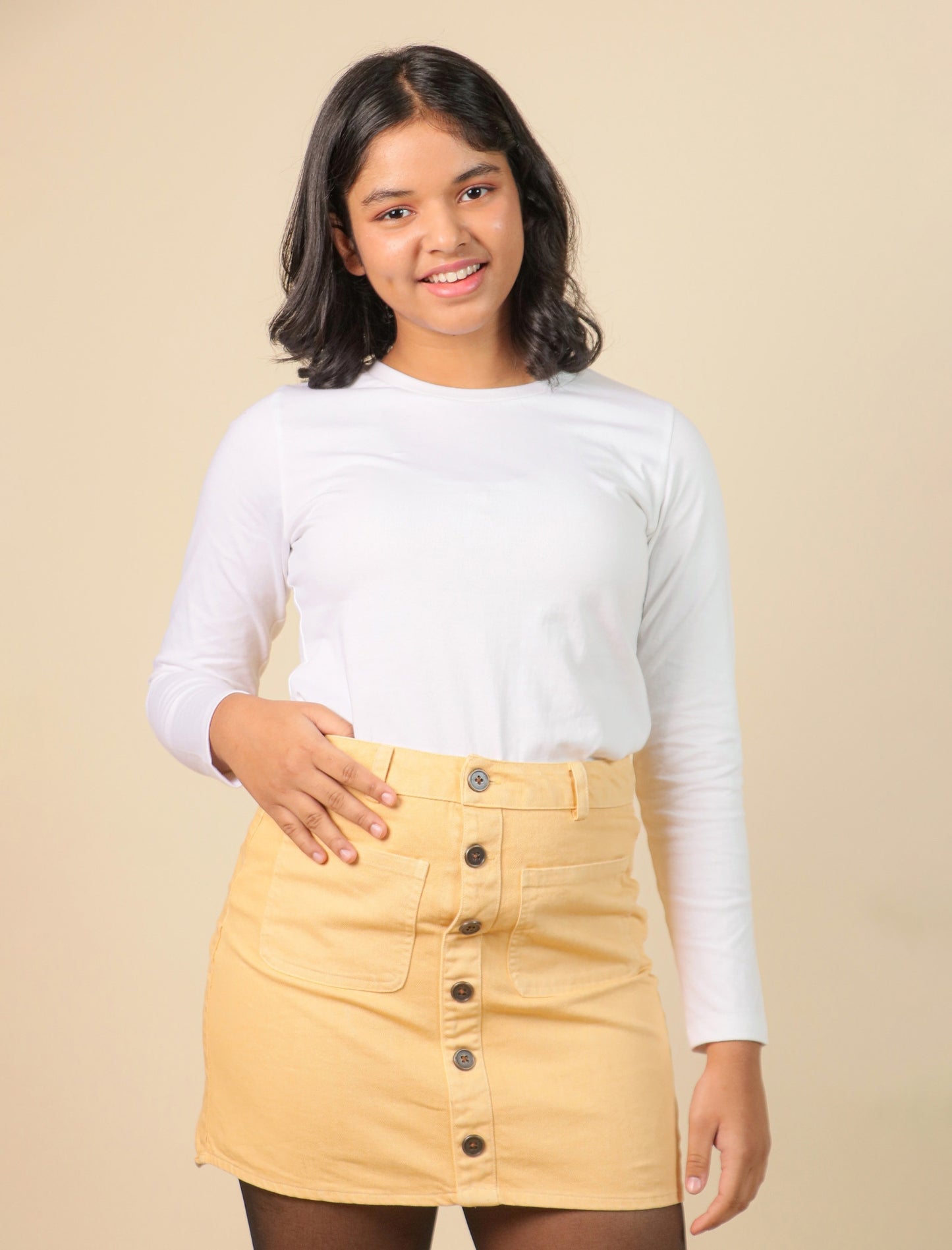 Girls wearing a white long-sleeve top and yellow skirt against a beige background