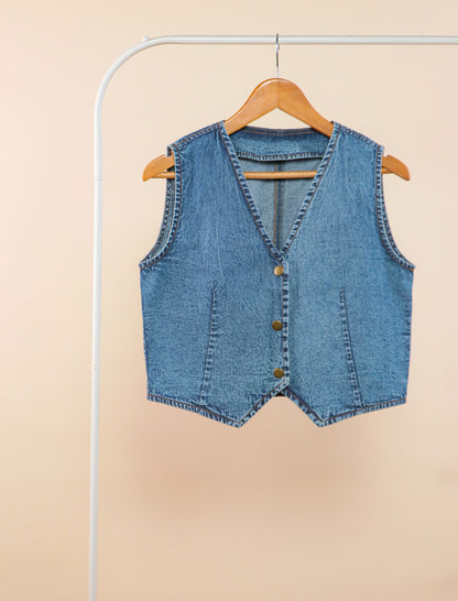 Blue denim vest on a hanger against a beige background