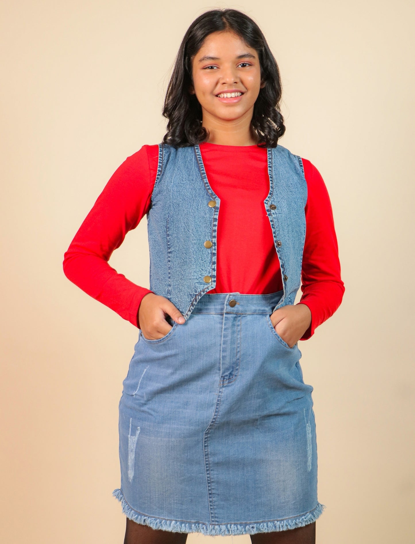 Girls wearing a red shirt, blue denim vest, and skirt against a beige background