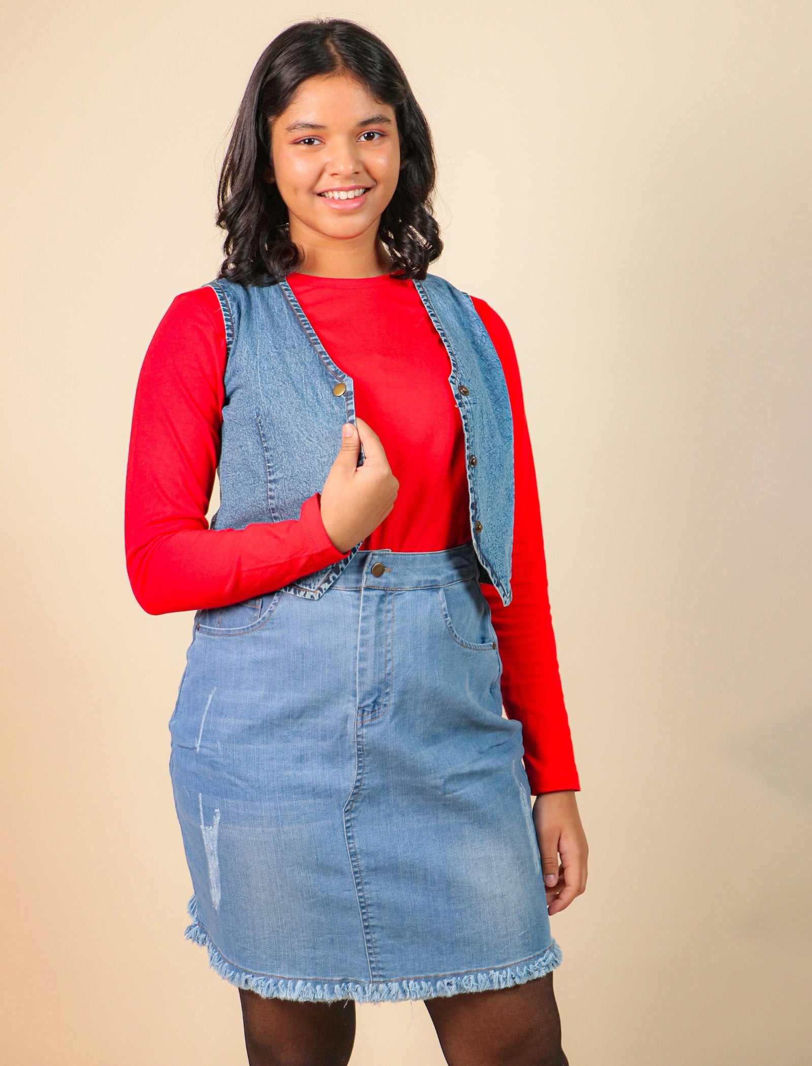 Girls wearing a red long-sleeve shirt, denim vest, and denim skirt against a beige background