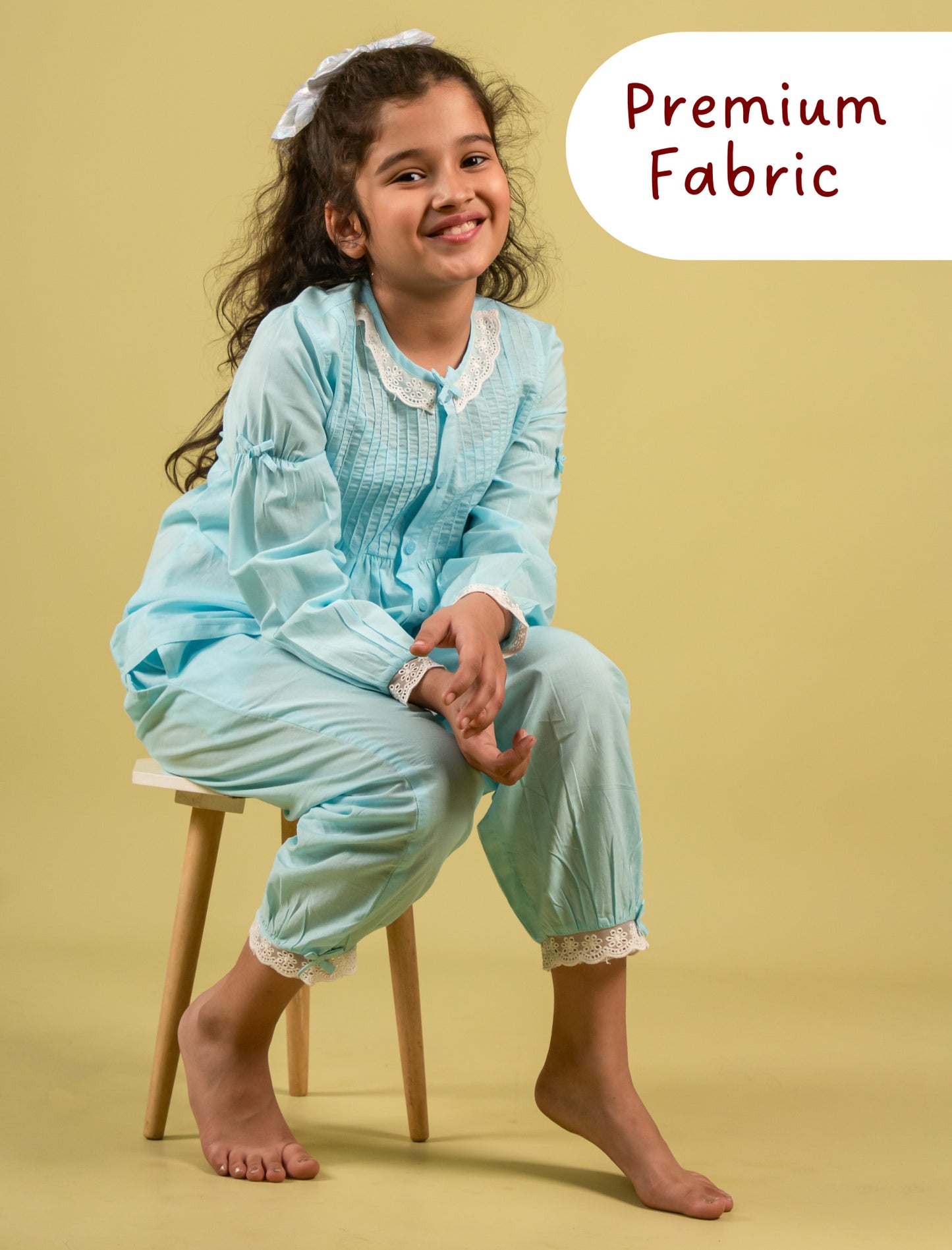 Girl wearing a light blue outfit sitting on a stool with 'Premium Fabric' text above.