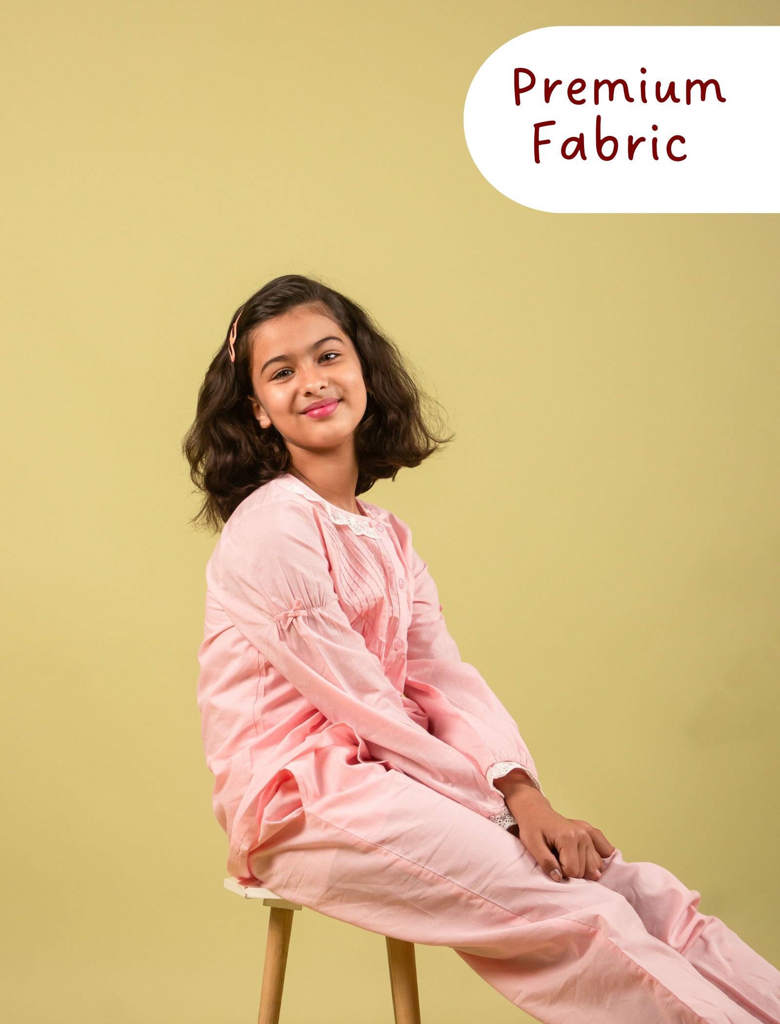 Young girl in a pink outfit sitting on a stool with 'Premium Fabric' text on a yellow background