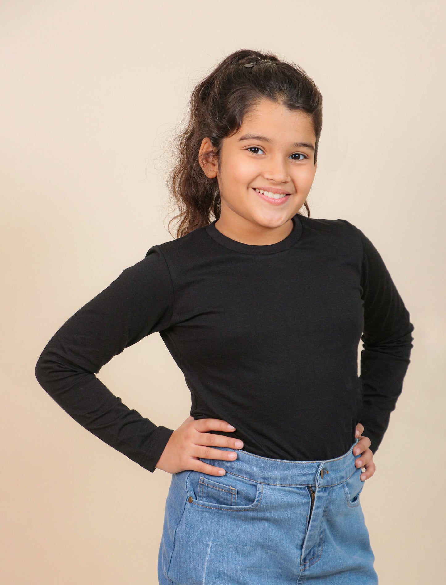 Girls wearing a black long-sleeve top and blue jeans against a beige background