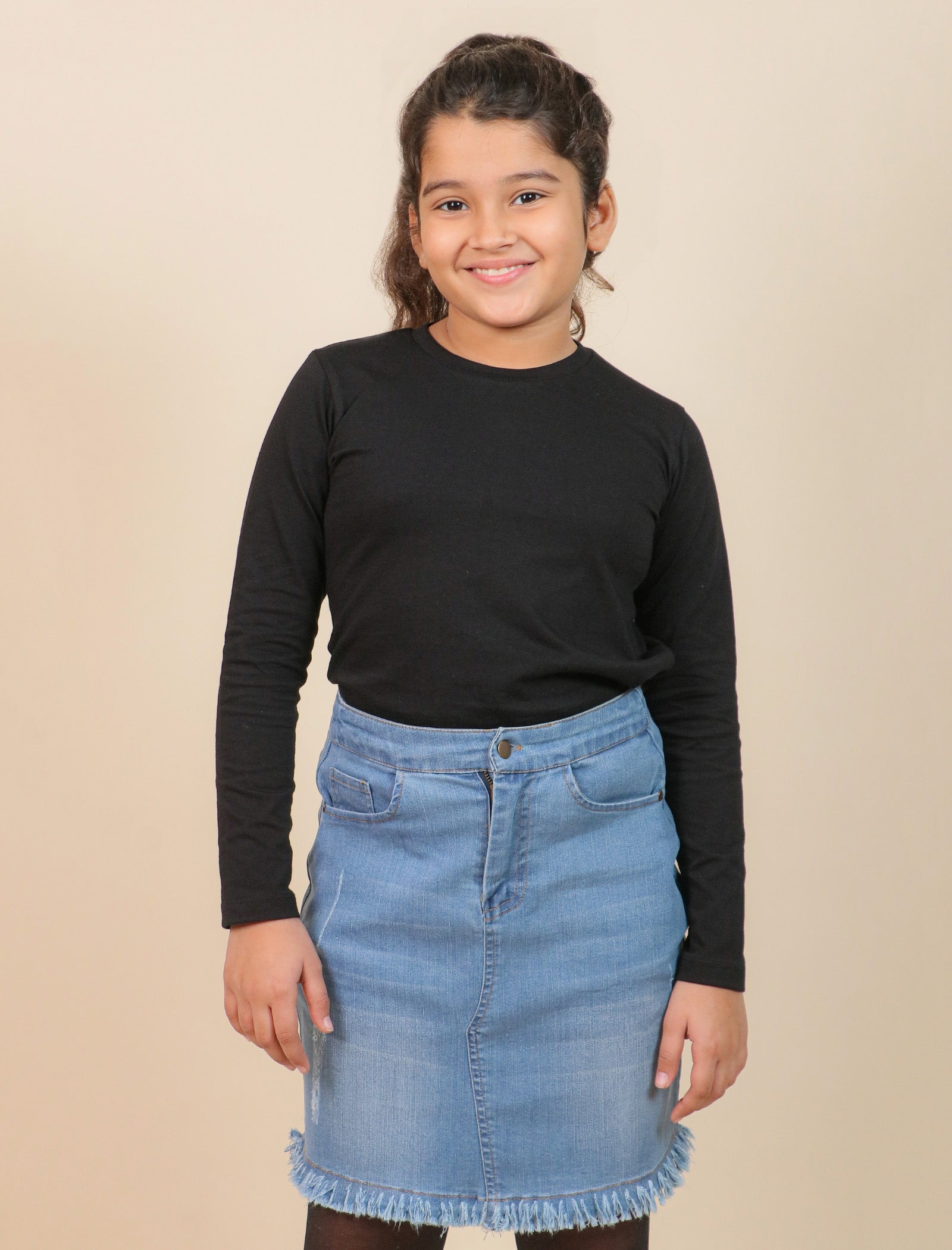 Girls wearing a black long-sleeve top and blue denim skirt against a beige background