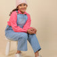 Girls wearing a pink hoodie, denim overalls, and white sneakers on a beige background