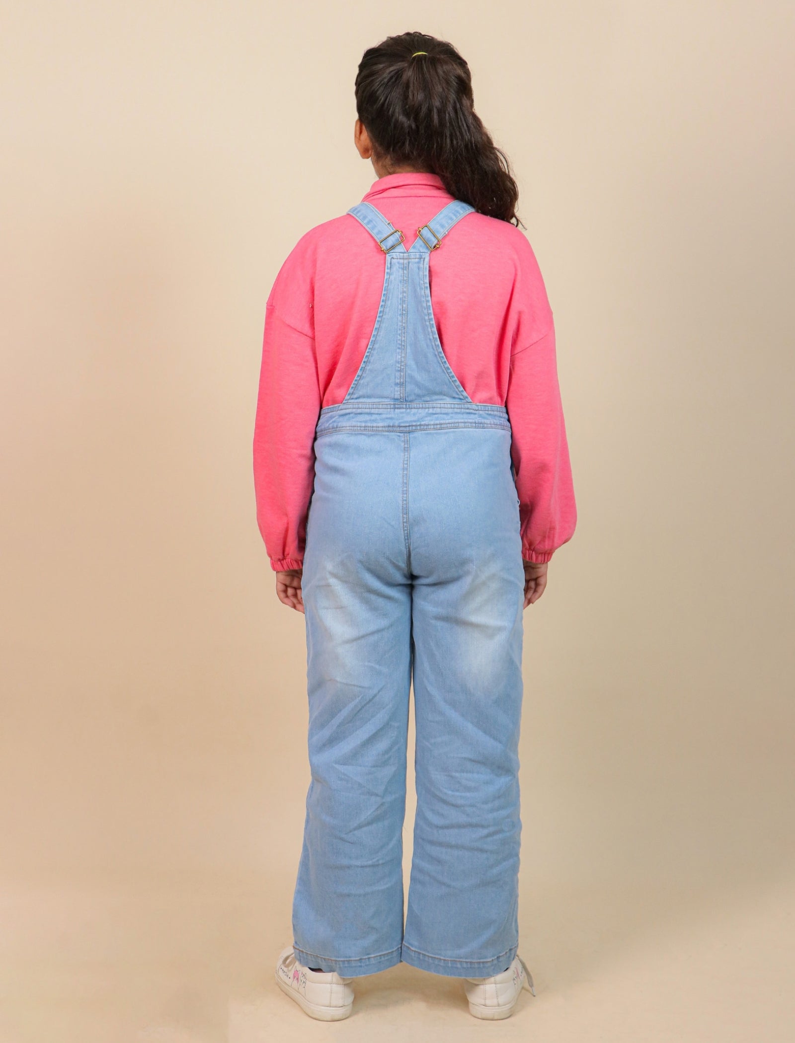 Girls wearing blue denim overalls and a pink shirt on a beige background
